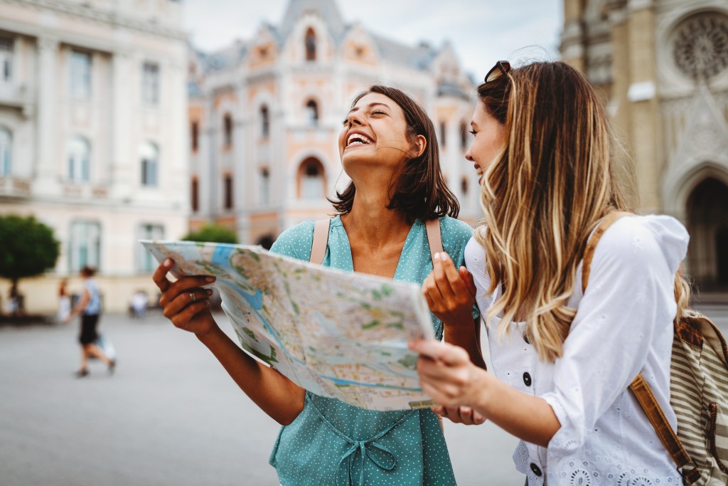 Dvi merginos keliauja, juokiasi ir varto žemėlapį.